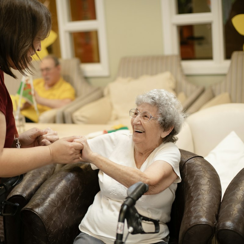 Aide à domicile tenant les mains d'une femme âgée souriante