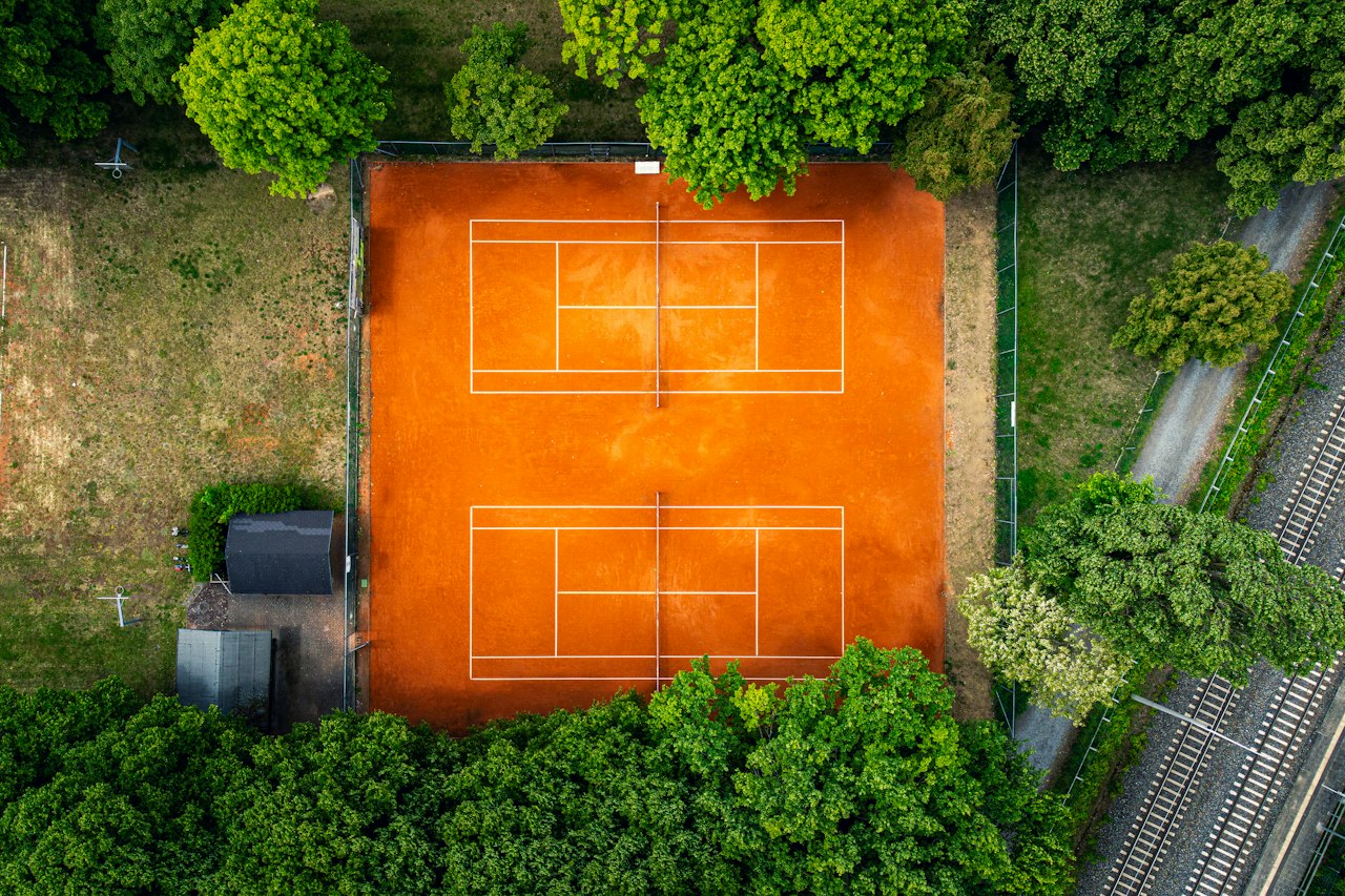 Court de tennis en terre battue entouré d'arbres, vu du ciel