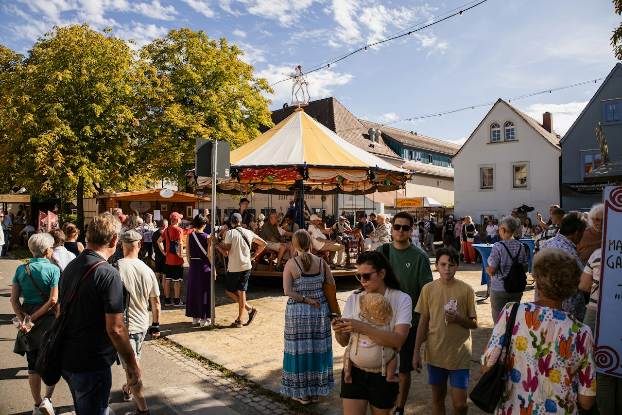 Foule réunie dans une rue de village lors d'une fête, avec un manège en arrière-plan