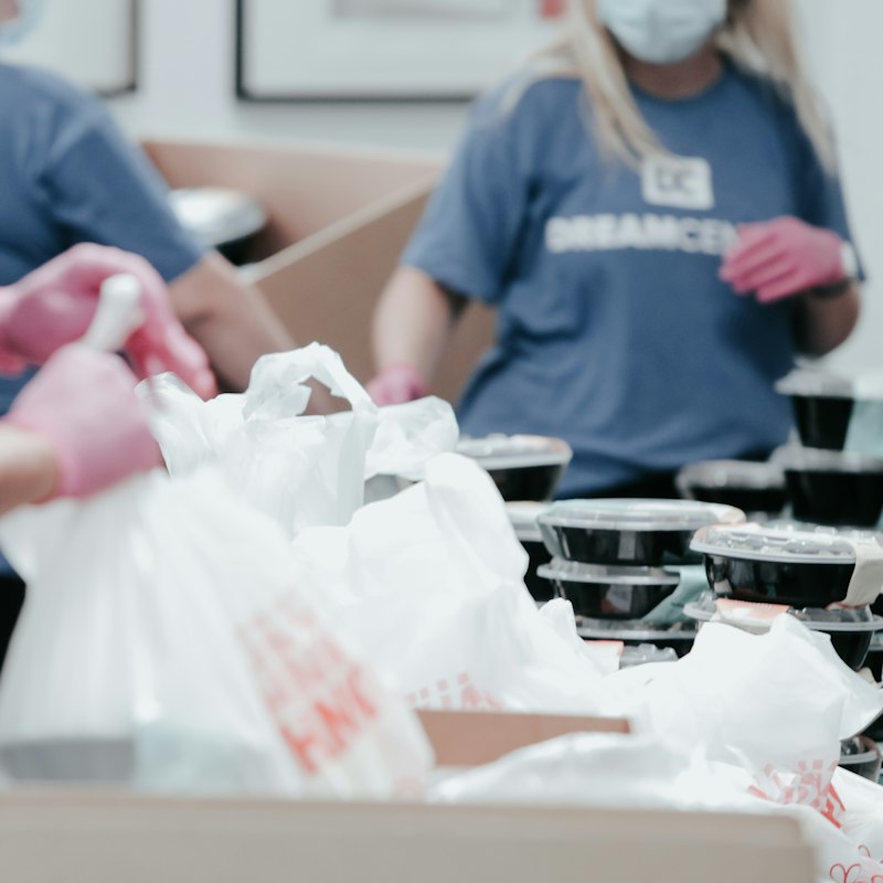 Bénévoles emballant des repas dans des sacs, gants roses aux mains