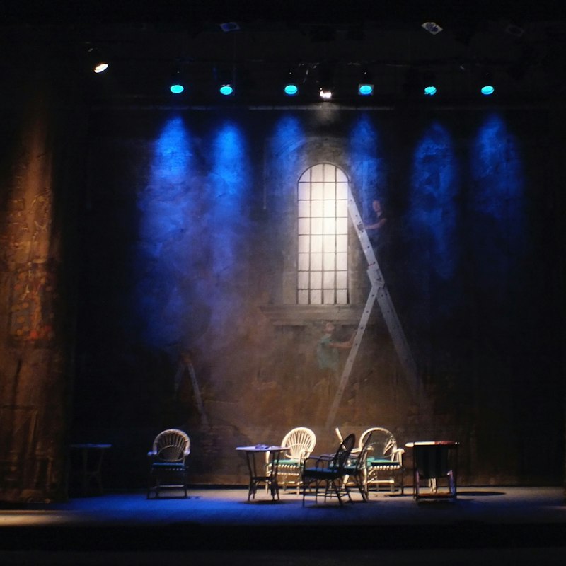 Scène de théâtre éclairée en bleu, décor et chaises prêts pour un spectacle