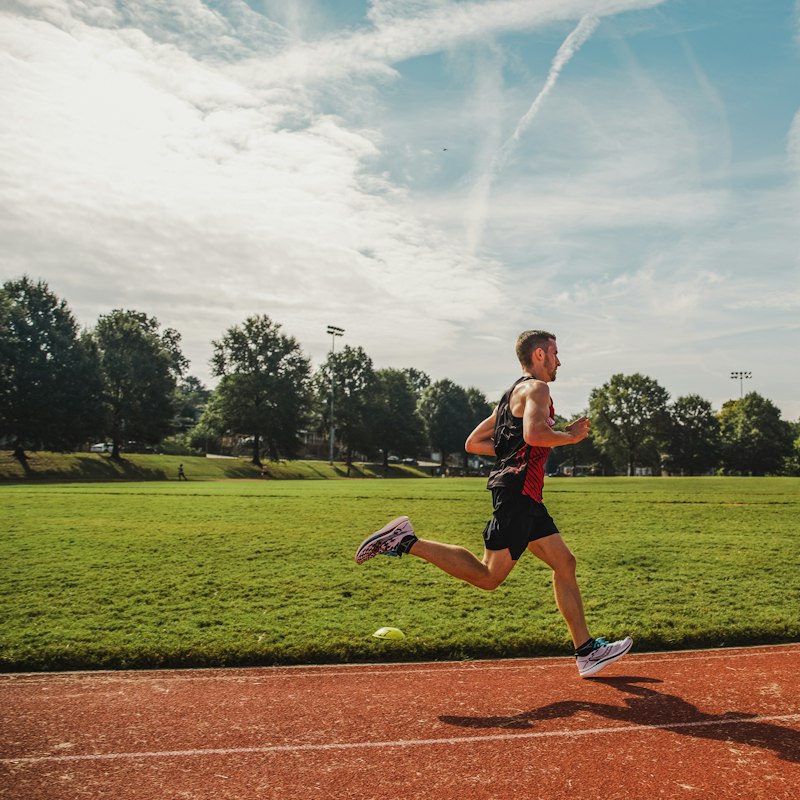 Coureur en action sur la piste d'un stade, devant la pelouse