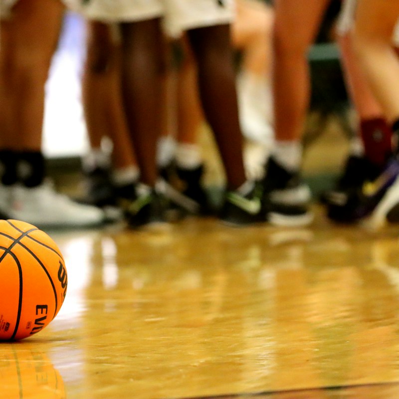 Ballon de basket orange sur un parquet, joueurs en arrière-plan