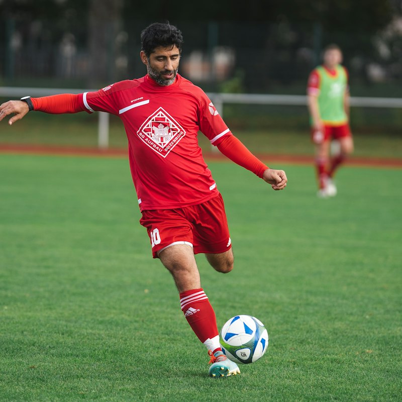 Joueur en maillot rouge frappant un ballon sur la pelouse