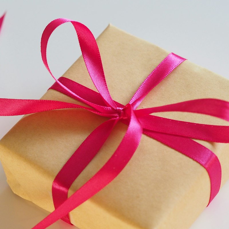 Un cadeau emballé dans du papier kraft avec un ruban rose